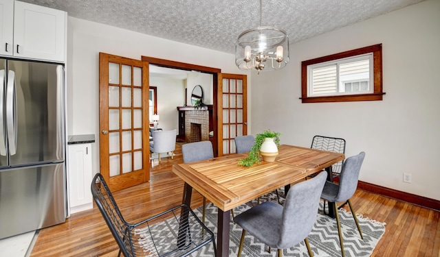 dining room featuring a fireplace, a chandelier, light hardwood / wood-style flooring, and a textured ceiling