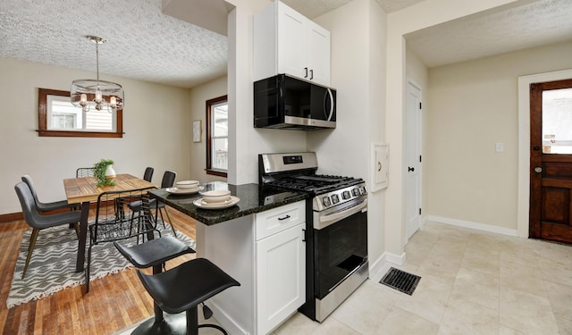 kitchen with a healthy amount of sunlight, decorative light fixtures, stainless steel range with gas stovetop, and white cabinets