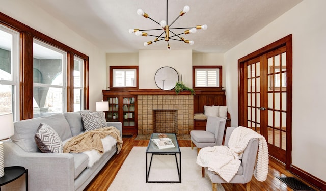 living room featuring french doors, a textured ceiling, a tile fireplace, a notable chandelier, and hardwood / wood-style floors