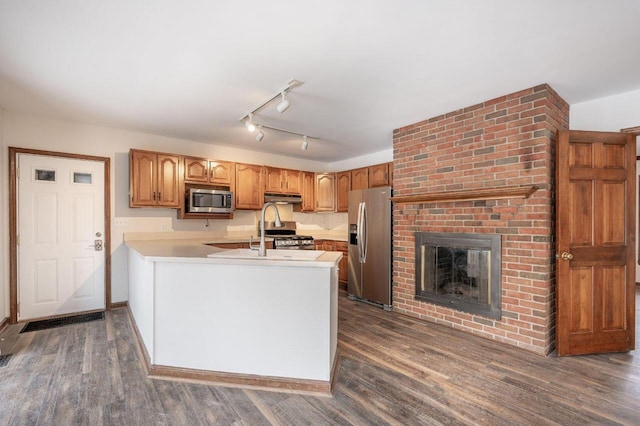 kitchen with a brick fireplace, appliances with stainless steel finishes, dark hardwood / wood-style floors, and kitchen peninsula