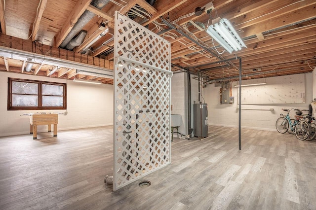 basement with water heater, hardwood / wood-style flooring, and electric panel