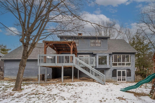 snow covered back of property featuring a playground and a deck