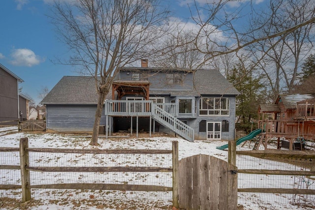 snow covered house featuring a wooden deck and a playground