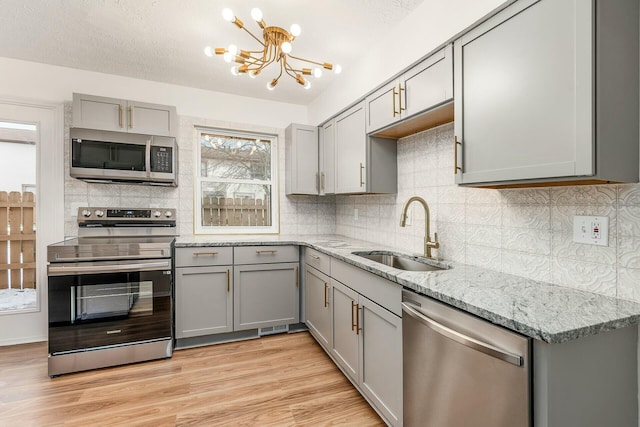 kitchen featuring appliances with stainless steel finishes, gray cabinets, sink, and light stone countertops