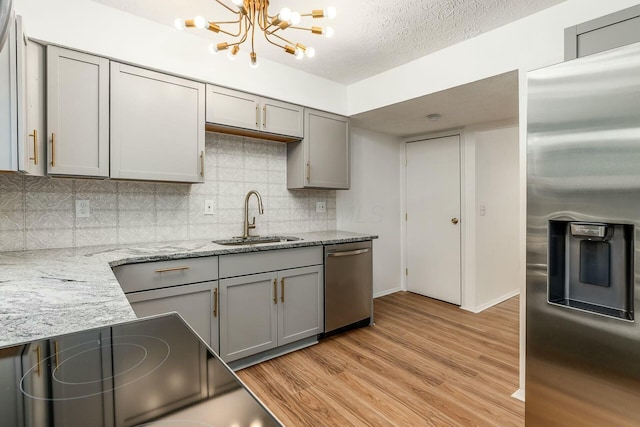 kitchen with gray cabinets, sink, light stone counters, stainless steel appliances, and light wood-type flooring