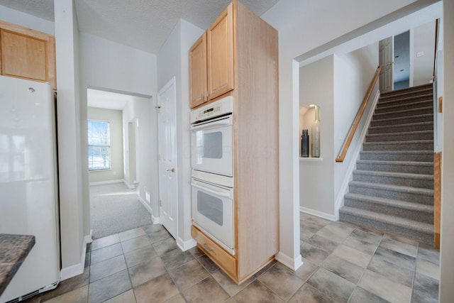 kitchen with white appliances, light brown cabinetry, light colored carpet, and a textured ceiling