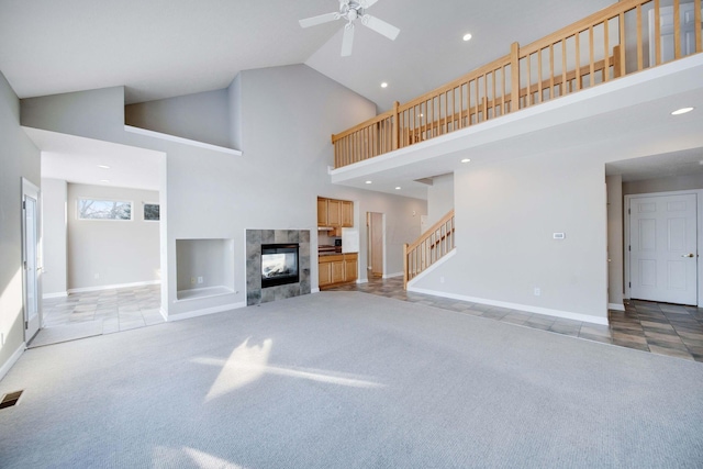 unfurnished living room featuring ceiling fan, a towering ceiling, a fireplace, and carpet flooring