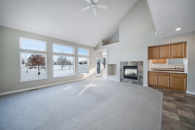 unfurnished living room with a tiled fireplace, ceiling fan, sink, and high vaulted ceiling