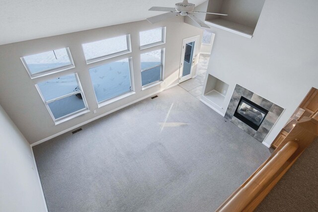 unfurnished living room featuring ceiling fan, light colored carpet, vaulted ceiling, and a tile fireplace