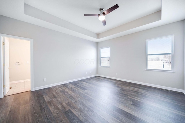 unfurnished room featuring dark hardwood / wood-style floors, ceiling fan, and a tray ceiling