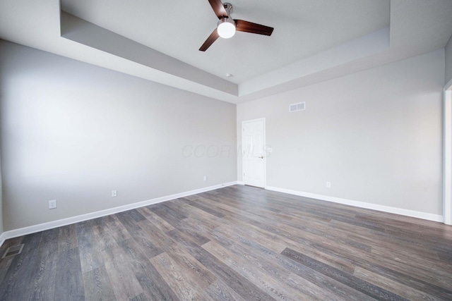 spare room with dark wood-type flooring, ceiling fan, and a raised ceiling