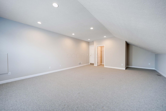 additional living space with lofted ceiling, light carpet, and a textured ceiling