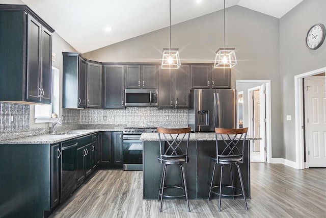 kitchen featuring appliances with stainless steel finishes, a center island, light stone counters, and decorative light fixtures