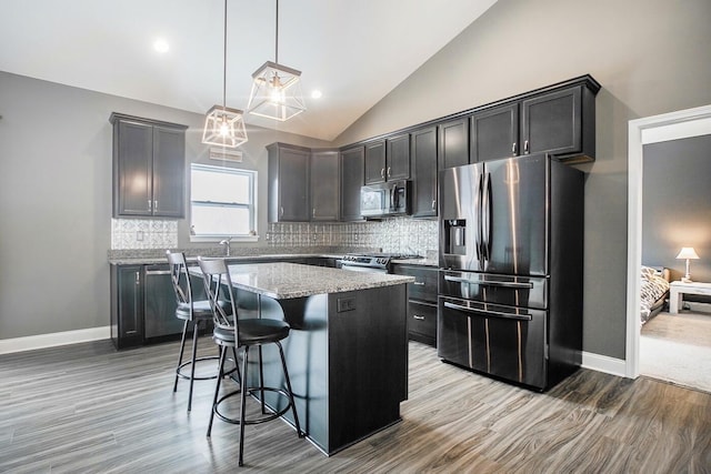 kitchen with appliances with stainless steel finishes, a kitchen breakfast bar, a center island, light stone counters, and decorative light fixtures