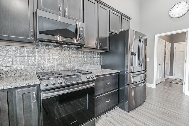 kitchen with stainless steel appliances, tasteful backsplash, light stone countertops, and light hardwood / wood-style floors