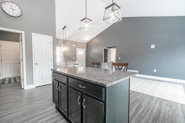 kitchen with light stone countertops, dark hardwood / wood-style floors, a center island, and hanging light fixtures