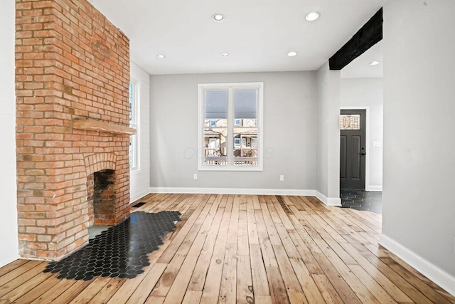 unfurnished living room with a brick fireplace, a wealth of natural light, and light hardwood / wood-style flooring