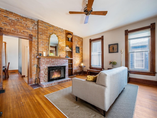 living room featuring ceiling fan, plenty of natural light, light wood-type flooring, and a fireplace