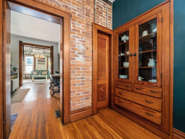 hall featuring an inviting chandelier, hardwood / wood-style flooring, and brick wall