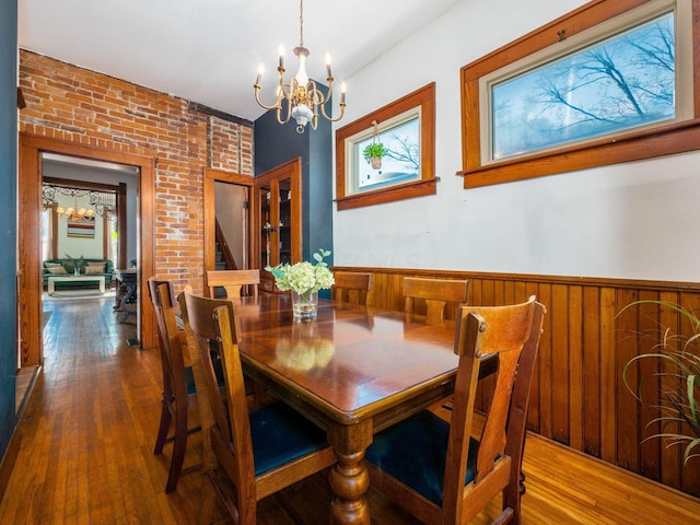 dining room with an inviting chandelier, brick wall, and dark hardwood / wood-style flooring