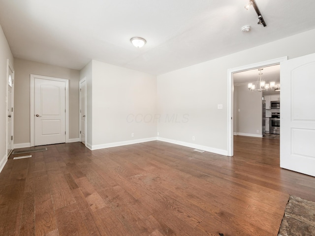 spare room featuring track lighting, a notable chandelier, and dark hardwood / wood-style flooring