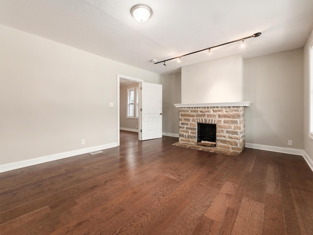 unfurnished living room featuring rail lighting, a brick fireplace, dark wood-type flooring, and a textured ceiling