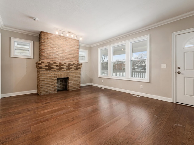 unfurnished living room featuring a brick fireplace, a textured ceiling, track lighting, ornamental molding, and dark hardwood / wood-style floors