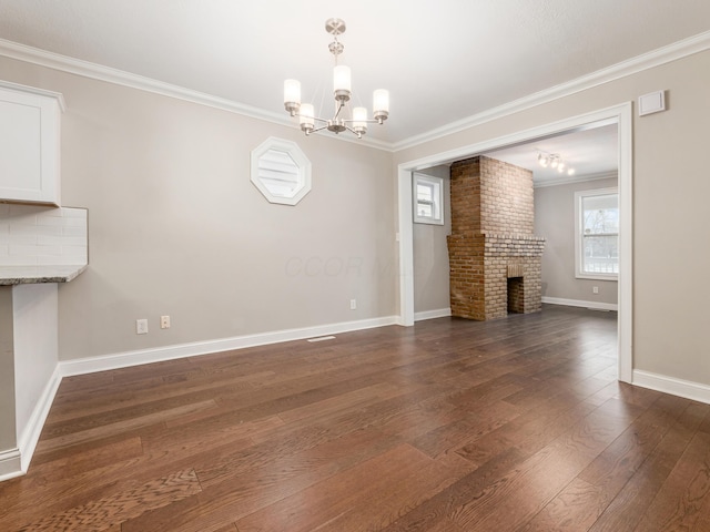 unfurnished living room featuring crown molding, a brick fireplace, dark wood-type flooring, and a notable chandelier