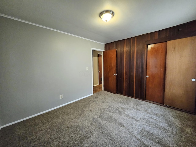 unfurnished bedroom with crown molding, carpet floors, a closet, and wood walls