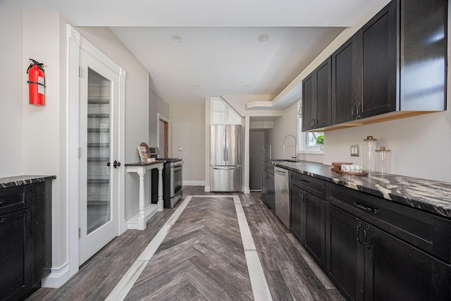 kitchen with dark stone countertops, sink, dark parquet flooring, and stainless steel appliances