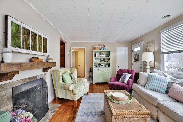 living room featuring a tiled fireplace, crown molding, and dark wood-type flooring