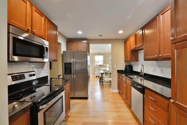 kitchen with appliances with stainless steel finishes, tasteful backsplash, sink, dark stone counters, and light hardwood / wood-style floors