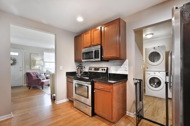 kitchen with stacked washer / dryer, dark stone countertops, stainless steel appliances, light hardwood / wood-style floors, and backsplash