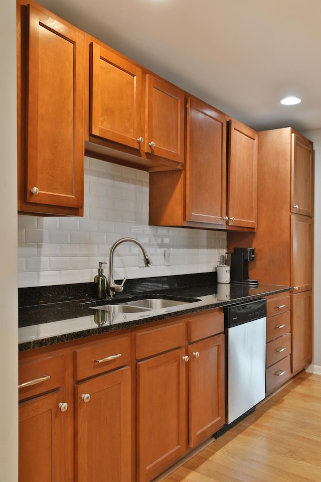 kitchen with sink, light hardwood / wood-style flooring, stainless steel dishwasher, dark stone counters, and decorative backsplash