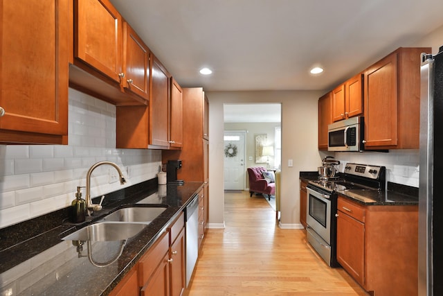 kitchen featuring dark stone countertops, sink, light hardwood / wood-style floors, and appliances with stainless steel finishes