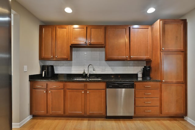 kitchen with sink, light wood-type flooring, dark stone counters, stainless steel appliances, and backsplash