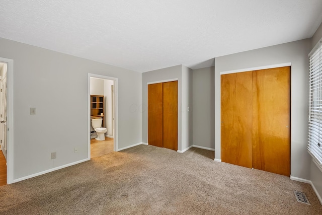 unfurnished bedroom with ensuite bathroom, a textured ceiling, and carpet flooring