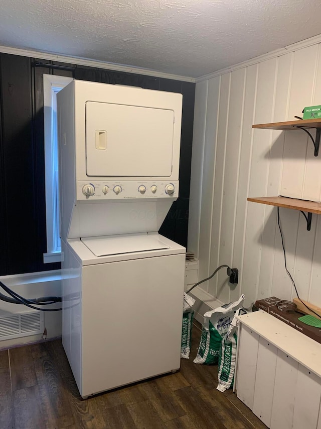 clothes washing area featuring dark wood-type flooring, stacked washer and dryer, crown molding, and a textured ceiling