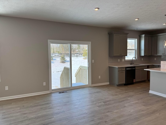 kitchen featuring sink, light wood-type flooring, dishwasher, gray cabinetry, and decorative backsplash