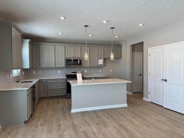 kitchen featuring sink, a center island, decorative light fixtures, stainless steel appliances, and gray cabinets