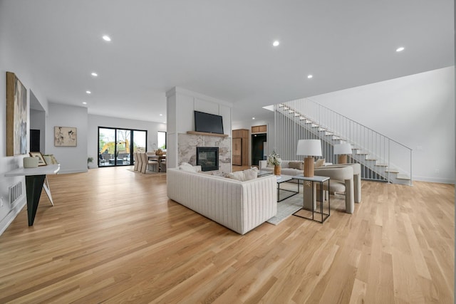 living room with a glass covered fireplace, stairway, light wood-style flooring, and recessed lighting