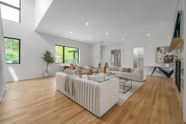living area with light wood-style flooring, baseboards, a stone fireplace, and recessed lighting