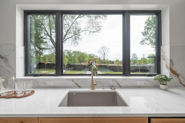 kitchen featuring light stone counters, brown cabinets, and a sink
