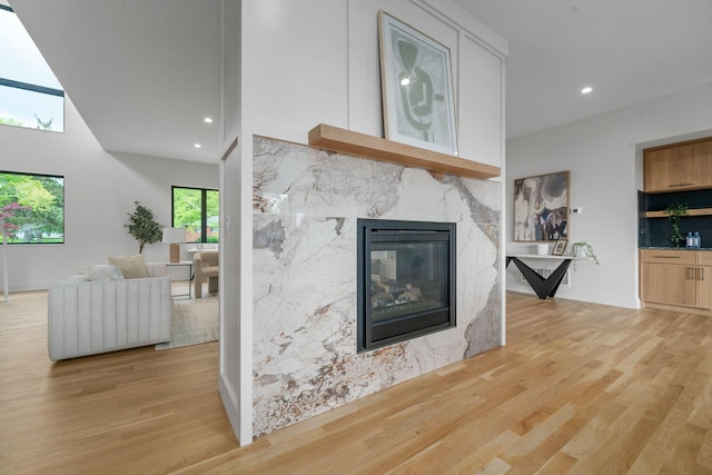 living area featuring baseboards, light wood-style floors, a high end fireplace, and recessed lighting