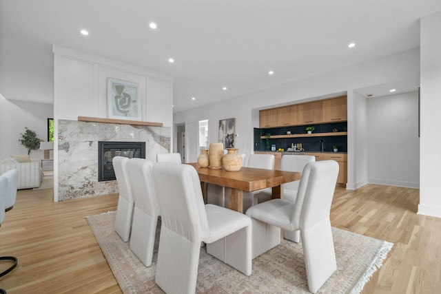 dining area with a premium fireplace, light wood-style flooring, baseboards, and recessed lighting