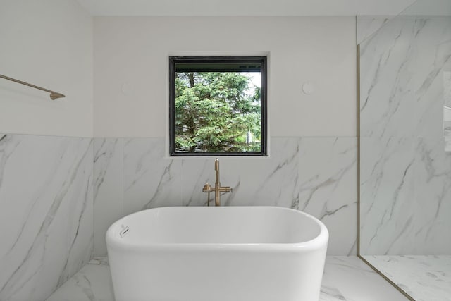 full bath featuring marble finish floor, tile walls, a freestanding bath, and a wainscoted wall