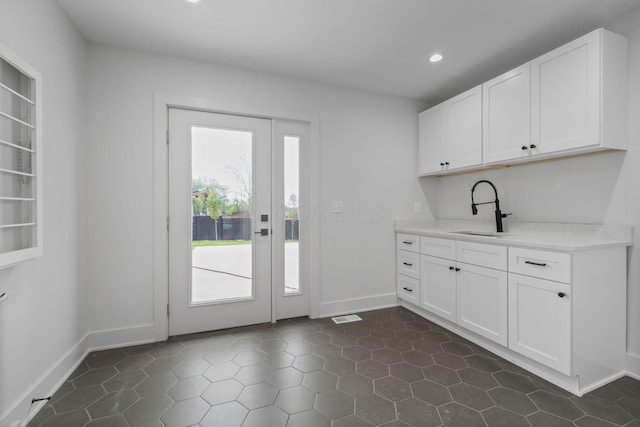 interior space with a sink, visible vents, white cabinetry, light countertops, and baseboards
