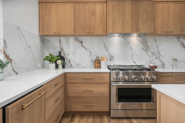 kitchen with brown cabinets, high end stainless steel range, backsplash, under cabinet range hood, and light wood-style floors
