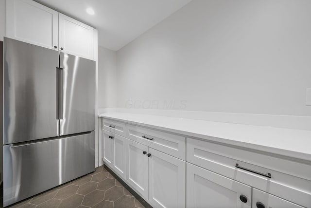 kitchen with white cabinets, light countertops, dark tile patterned flooring, and stainless steel fridge