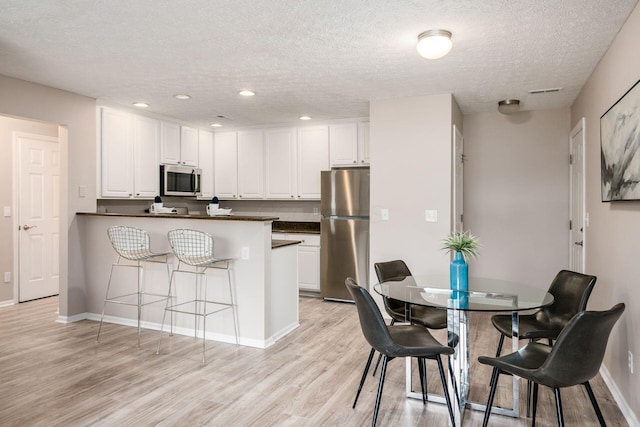 kitchen with a kitchen bar, light wood-type flooring, kitchen peninsula, stainless steel appliances, and white cabinets